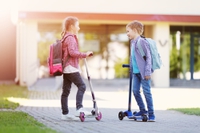 Girl and boy standing with scooters at school and talking together.