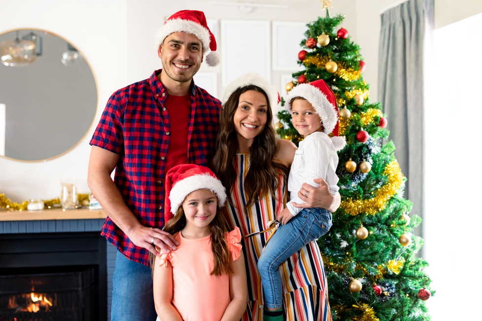 Family_Wears_Santa_Hats_While_Standing_In_Front_Of_The_Christmas_Tree_original_3523761.jpg